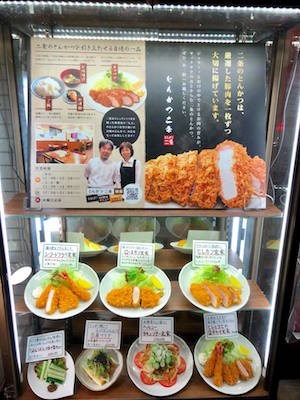 とんかつ屋の店頭看板のアップ。メニュー写真や店主の写真が見える